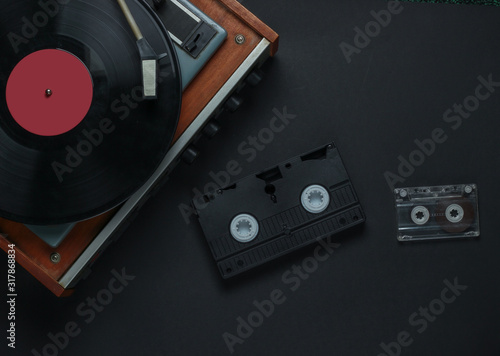 Flat lay retro media and entertainment. Vinyl record player with vinyl record, audio cassette, vhs on black background. 80s. Top view