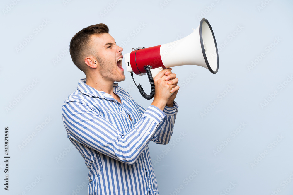 Young handsome blonde man over isolated blue background shouting through a megaphone Young handsome blonde man over isolated blue background shouting through a megaphone