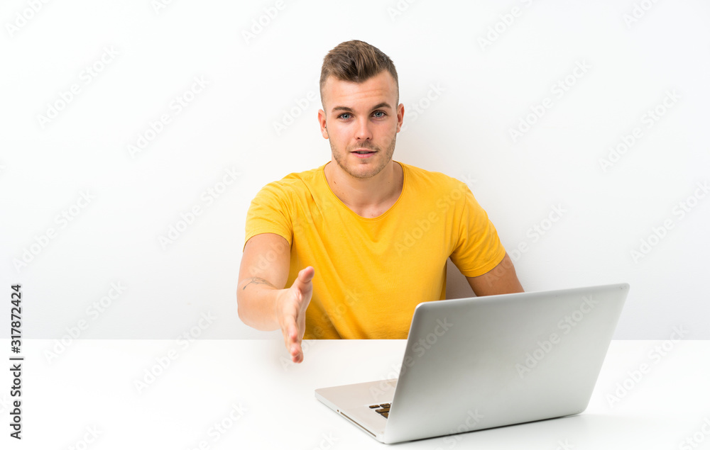 Young blonde man in a table with a laptop handshaking after good deal Young blonde man in a table with a laptop handshaking after good deal