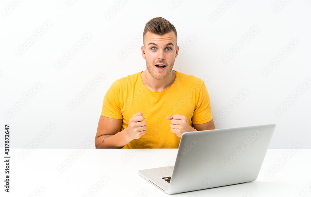 Young blonde man in a table with a laptop celebrating a victory Young blonde man in a table with a laptop celebrating a victory
