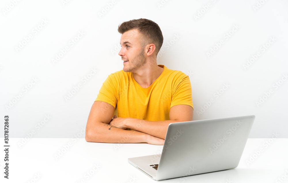 Young blonde man in a table with a laptop looking to the side Young blonde man in a table with a laptop looking to the side