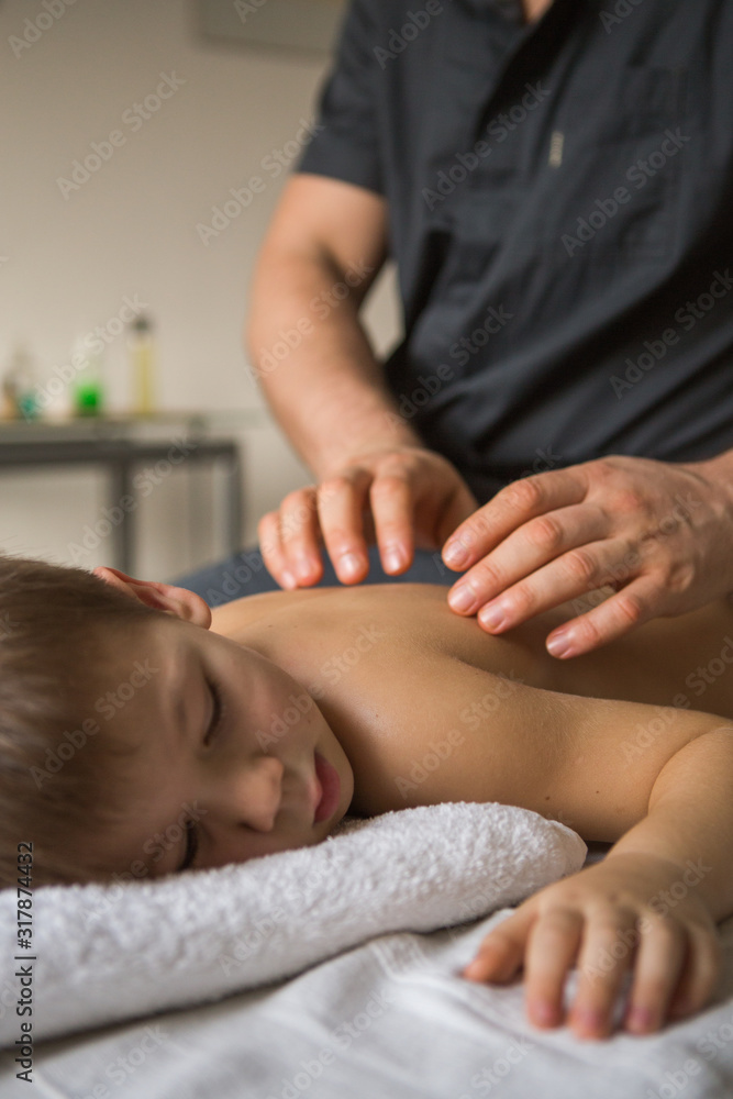 Boy toddler relaxes from a therapeutic massage. Physiotherapist working with patient in clinic to the back of a child Boy toddler relaxes from a therapeutic massage. Physiotherapist working with patient in clinic to the back of a child