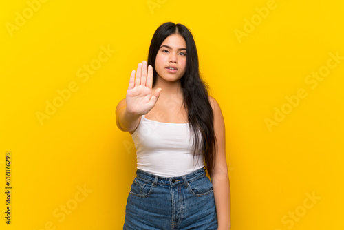 Young teenager Asian girl over isolated yellow background making stop gesture