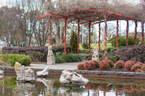 A small local park with red Chinese-style decoration. A lake with decorative stones and stone column. Shepparton, Australia.