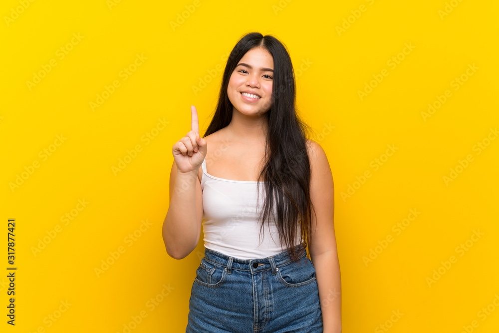 Young teenager Asian girl over isolated yellow background showing and lifting a finger in sign of the best Young teenager Asian girl over isolated yellow background showing and lifting a finger in sign of the best