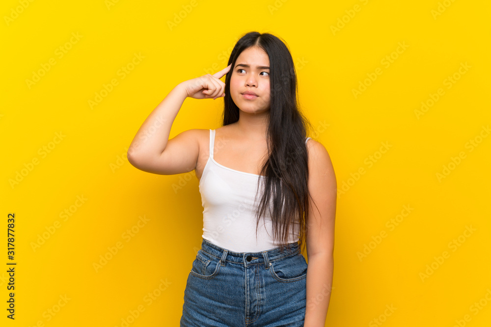Young teenager Asian girl over isolated yellow background making the gesture of madness putting finger on the head Young teenager Asian girl over isolated yellow background making the gesture of madness putting finger on the head