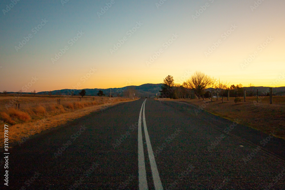 An empty road through New South Wales (NSW) in the twilight goes to the mountain in the centre. Australia.
