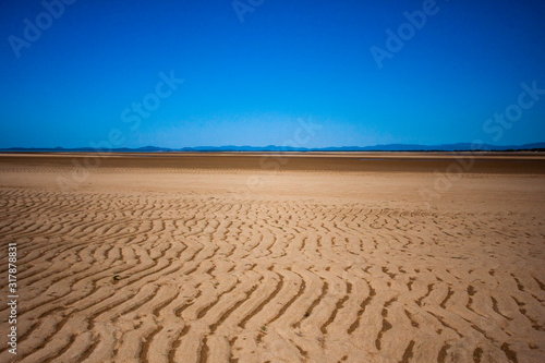 The coastal strip  coastline  beach  at low tide. A wide strip of desert sand to the horizon  a desert area  a wavy relief runs along it. Makey  Queensland  Australia.