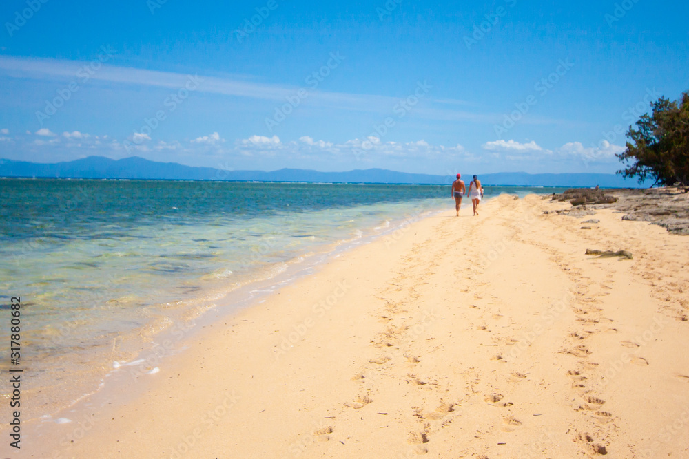 A couple, man and women, goes along the wide sandy beach. Green island, Queensland, Australia.