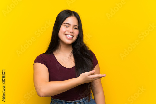 Young teenager Asian girl over isolated yellow background extending hands to the side for inviting to come