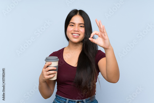 Young teenager Asian girl holding a take away coffee showing ok sign with fingers