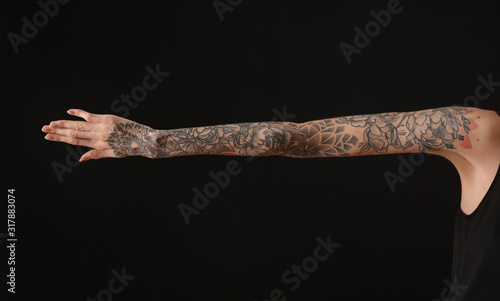 Woman with colorful tattoos on arm against black background, closeup