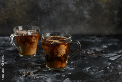 Ice coffee in a glass cups with cream poured over and coffee beans . Cold summer drink on a dark background with copy space for text..