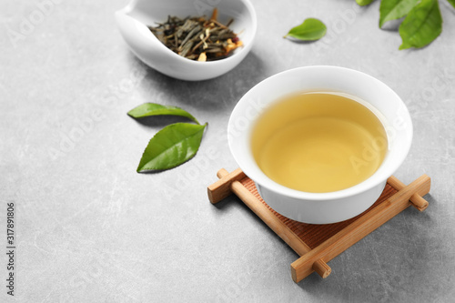 Cup of green tea, dry and fresh leaves on grey table. Space for text