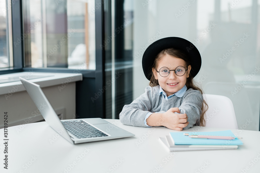 Cute smiling schoolgirl in eyeglasses and casualwear preparing homework Cute smiling schoolgirl in eyeglasses and casualwear preparing homework