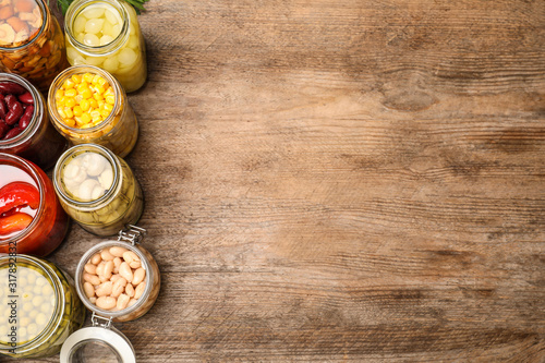 Glass jars with different pickled vegetables on wooden table, flat lay. Space for text