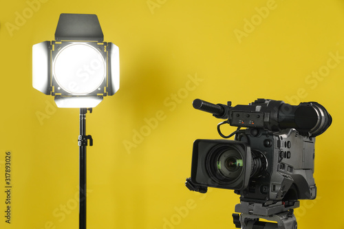Professional video camera and lighting equipment on yellow background