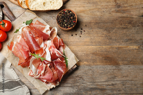 Pile of tasty prosciutto on wooden table, flat lay. Space for text