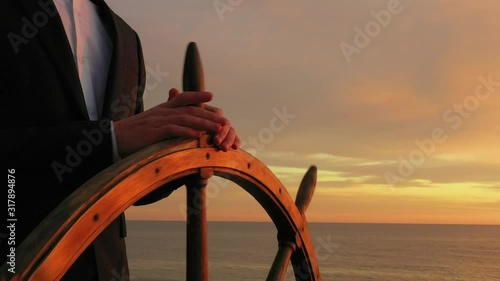 Businessman holding ship rudder and steers in sunset light.