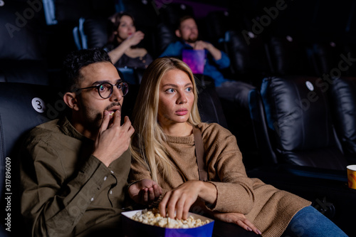 Young scared dates with box of popcorn watching horror movie at leisure