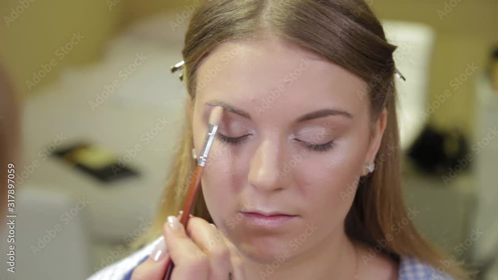 Professional make-up artist with a brush applies eye shadow to a client in a beauty salon. Professional make-up artist with a brush applies eye shadow to a client in a beauty salon.