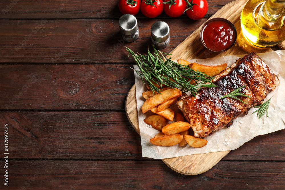 Delicious grilled ribs and garnish on wooden table, flat lay. Space for text