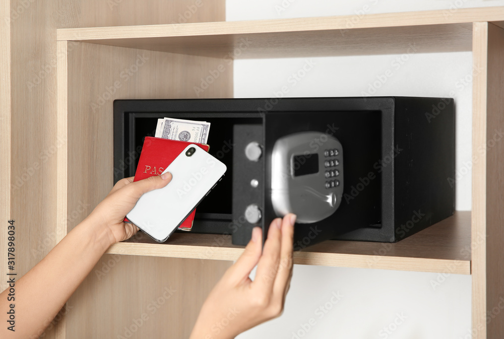 Woman putting smartphone, passport and money into steel safe, closeup Woman putting smartphone, passport and money into steel safe, closeup