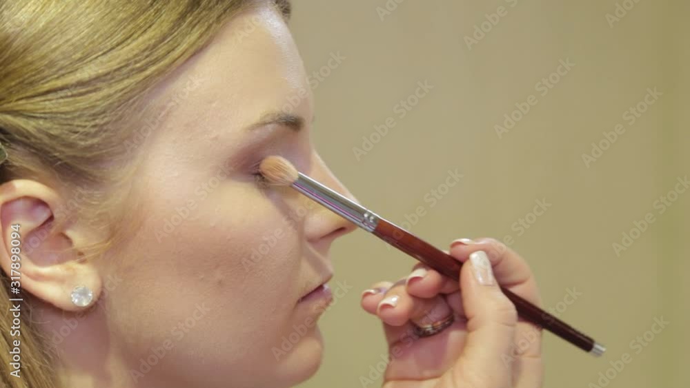 Professional make-up artist with a brush applies eye shadow to a client in a beauty salon.