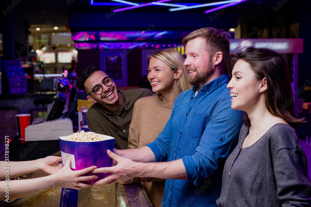 Obraz premium Two happy young couples buying popcorn by cashier counter before movie