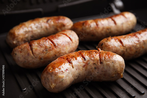 Cooking delicious sausages on modern grill, closeup
