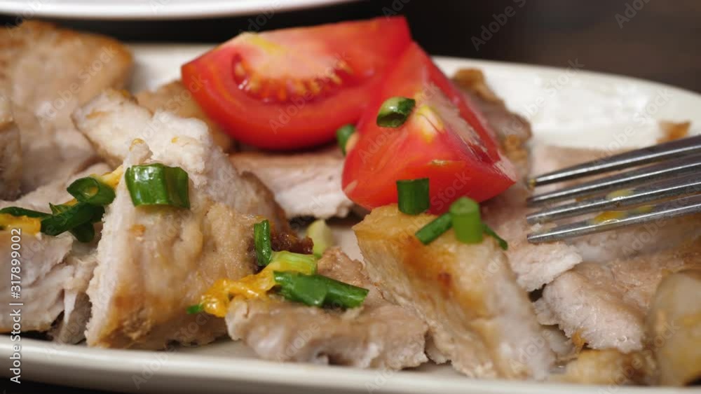 Cut pieces of cooked pork with red tomatoes and chopped green onion and fork rotate on white rectangular plate. Brown wooden background Cut pieces of cooked pork with red tomatoes and chopped green onion and fork rotate on white rectangular plate. Brown wooden background