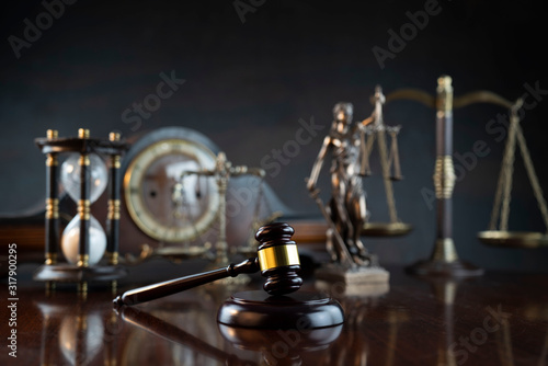Law and justice theme. Judge’s gavel, Themis statue, scale, hourglass and old clock on the shining wooden brown table and the gray background.