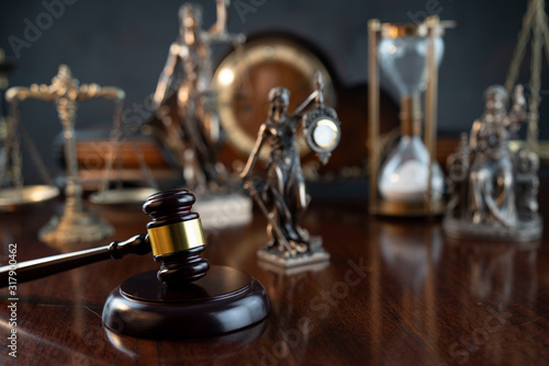 Law and justice theme. Judge’s gavel, Themis statue, scale, hourglass and old clock on the shining wooden brown table and the gray background.