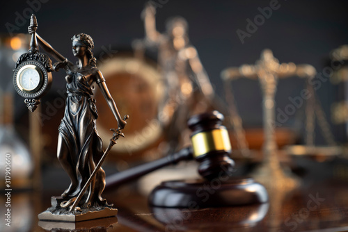 Law and justice theme. Judge’s gavel, Themis statue, scale, hourglass and old clock on the shining wooden brown table and the gray background.