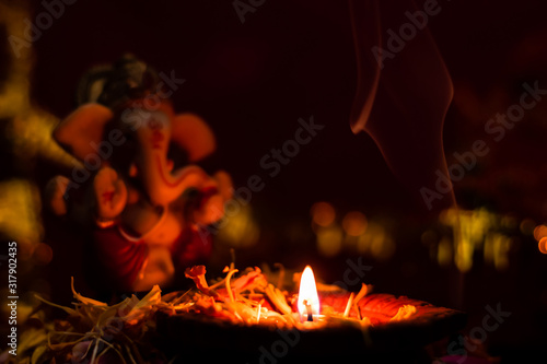 close up of glowing earthen lamp against blurry ganesha statue with dark background. hinduism concept.