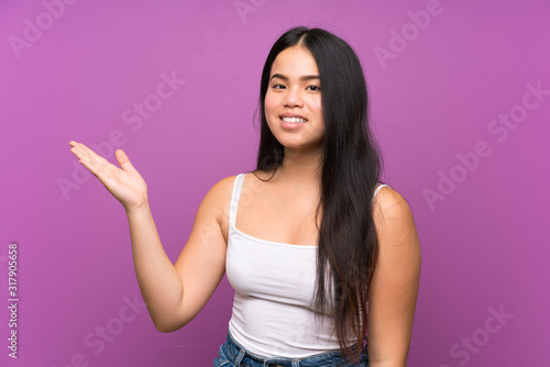Young teenager Asian girl over isolated purple background holding copyspace imaginary on the palm