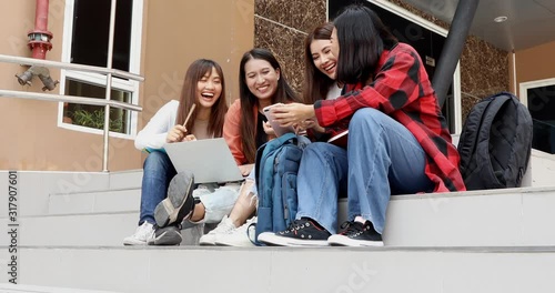 A group of Asian girl students taking a break from doing their report by watching video from mobile phone in their free time in school.