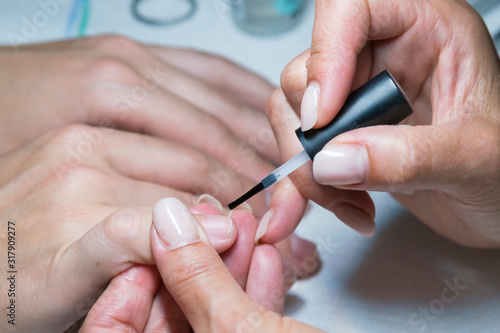 woman hand on manicure treatment with cuticle knife in beauty salon. applying a brush on acrylic nails in the salon