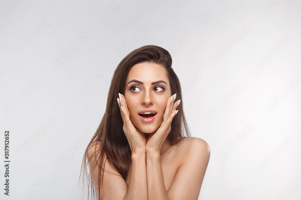 Fototapeta premium Beautiful woman portrait surprise holds cheeks by hand .Beautiful girl with long hair surprised and shocked looking aside . Presenting your product. Expressive facial expressions
