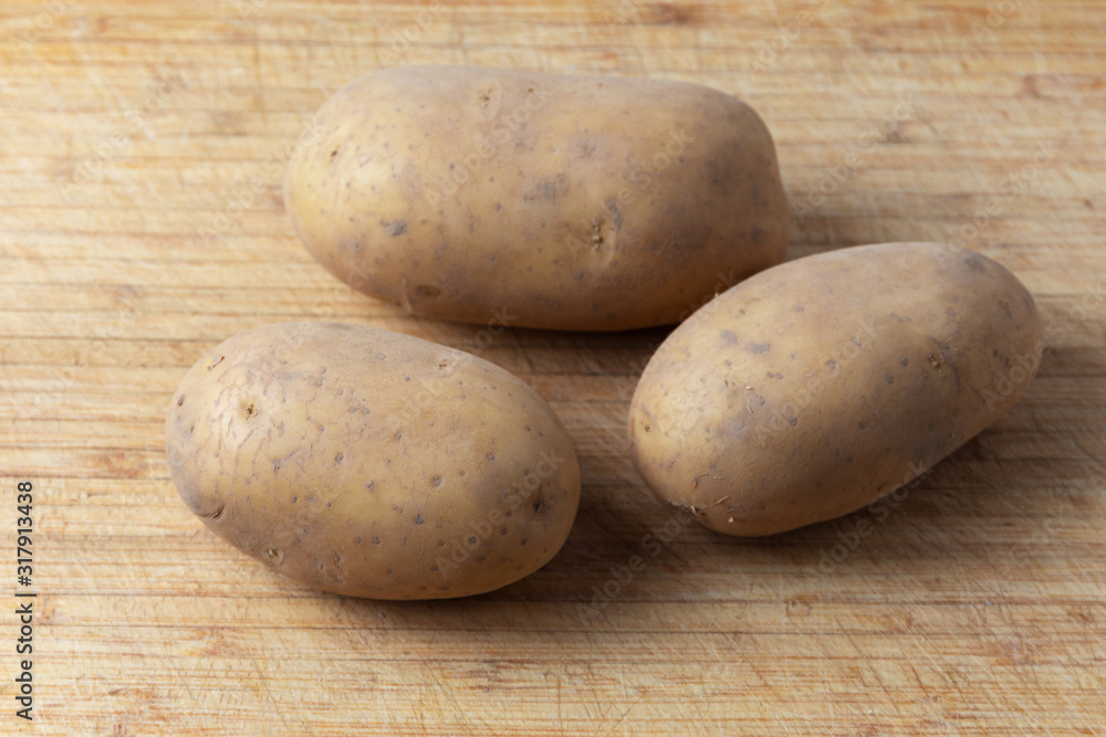 unpeeled potatoes on a  wooden board