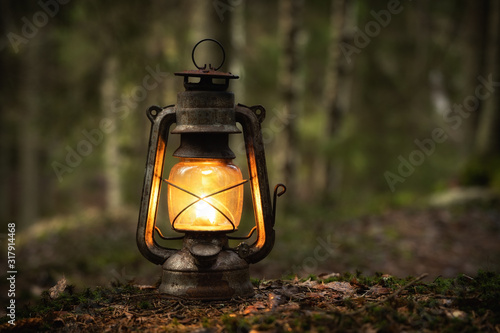 Vintage old lantern lighting in the dark forest. Travel camping concept. Burning lantern on a moss at forest in the night.
