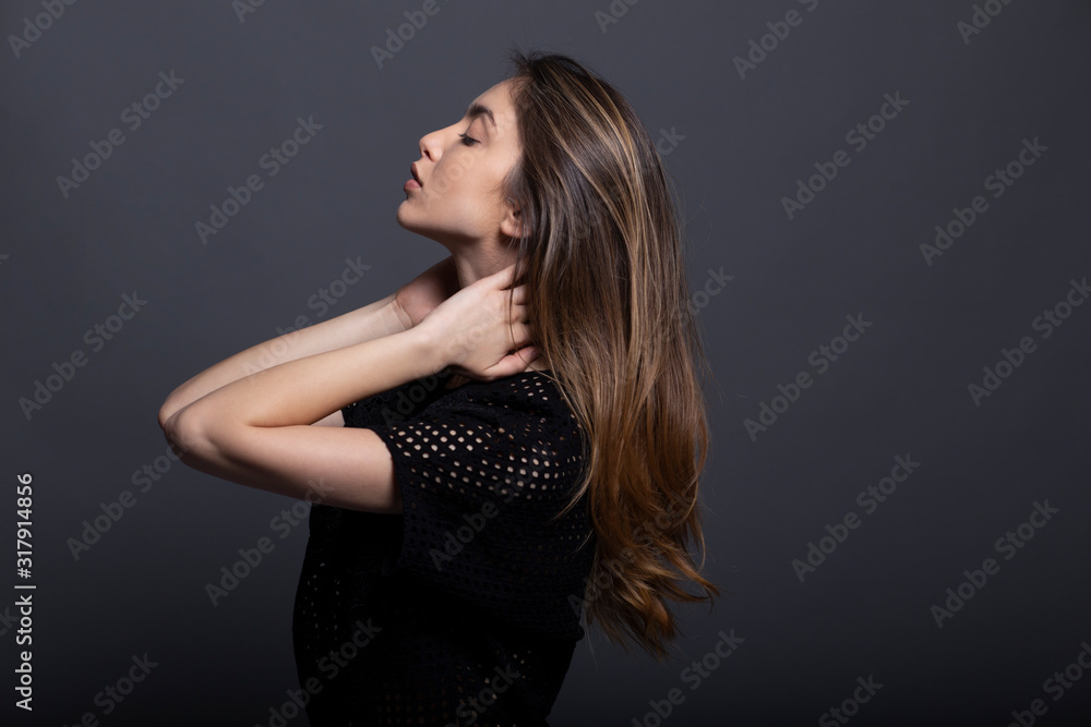 Portrait in profile of a confident beautiful girl with natural makeup, holding her hands behind neck, isolated on a grey background. Portrait in profile of a confident beautiful girl with natural makeup, holding her hands behind neck, isolated on a grey background.