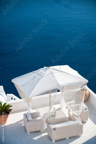 Quintessential Greek island scene of bright white umbrella and deck furniture overlooking smooth blue Mediterranean Sea in Santorini  Greece