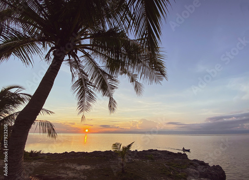 The magical landscape of a beautiful sunrise  sunset. Palm tree standing on a rocky coast. A man floating in a boat on the sea