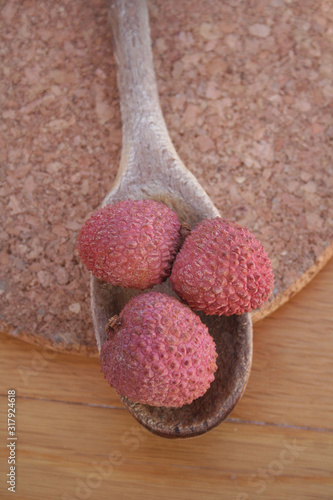 Fresh ripe litchi or lychee fruits on wooden spoon on wooden table. Litchi chinensis fruit on table
