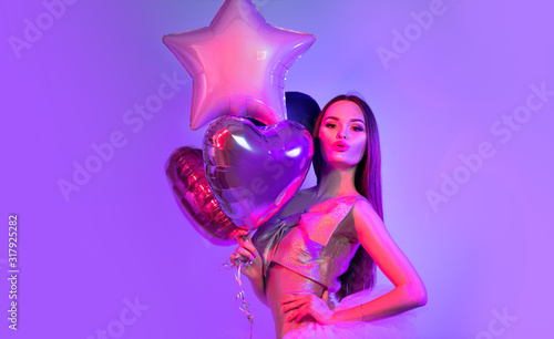 Valentine Beauty girl air balloons laughing in neon lights, on ultra violet background. Beautiful Happy Young woman, holiday party. Joyful model posing, having fun, celebrating  Valentine's Day