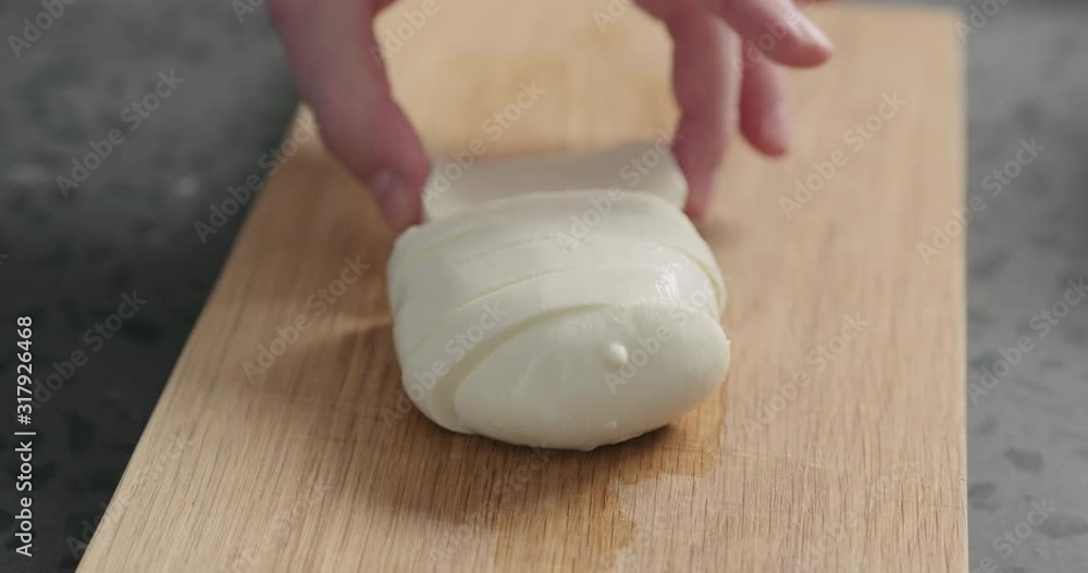 Closeup slow motion man slicing fresh mozzarella on oak board Closeup slow motion man slicing fresh mozzarella on oak board