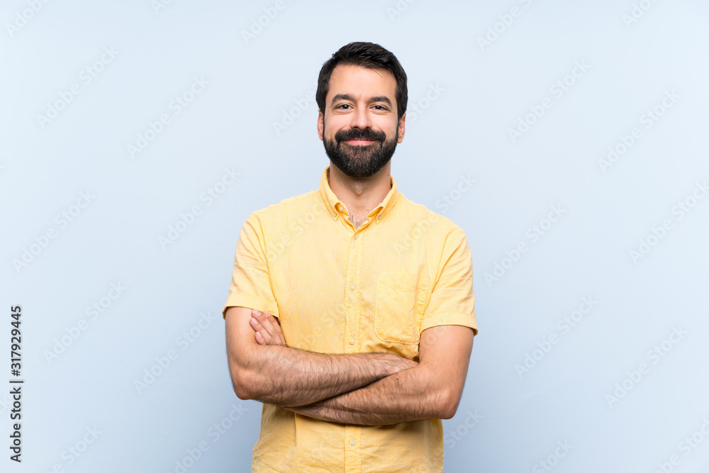 Young man with beard over isolated blue background keeping the arms crossed in frontal position Young man with beard over isolated blue background keeping the arms crossed in frontal position