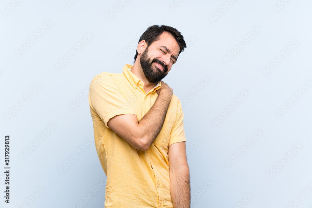 Naklejka premium Young man with beard over isolated blue background suffering from pain in shoulder for having made an effort
