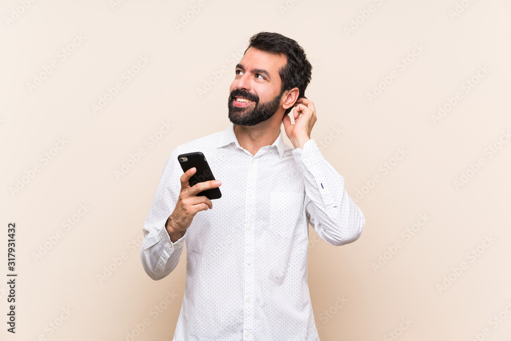 Young man with beard holding a mobile thinking an idea Young man with beard holding a mobile thinking an idea